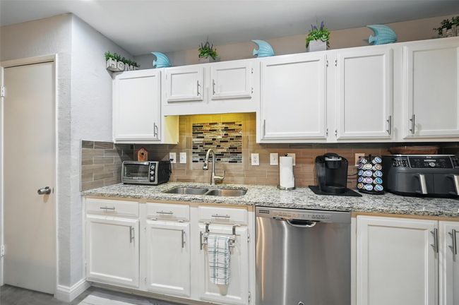 Kitchen with dishwasher, decorative backsplash, white cabinetry, and light stone countertops | Image 16