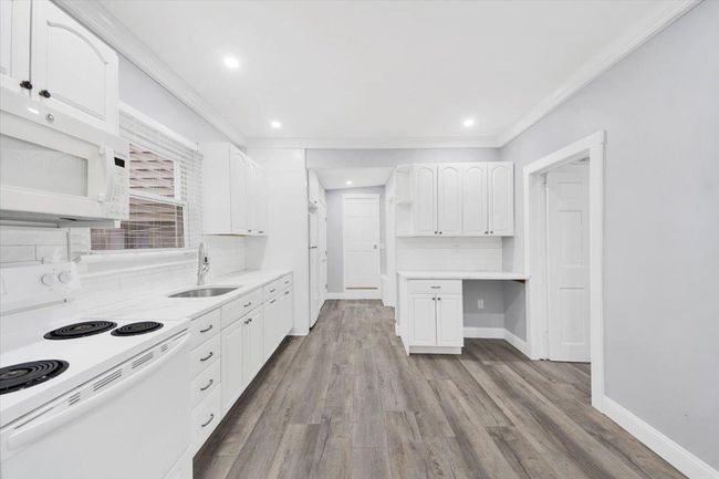 Kitchen featuring white appliances, a sink, white cabinetry, decorative backsplash, and ornamental molding | Image 7