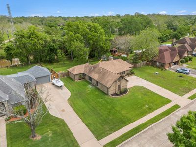 An aerial view shows the street view with sidewalks, deep front yard and mature trees in the backyard. | Image 2