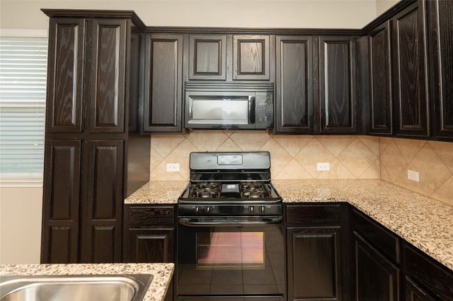 Kitchen with black appliances, backsplash, light stone countertops, and dark brown cabinets | Image 33