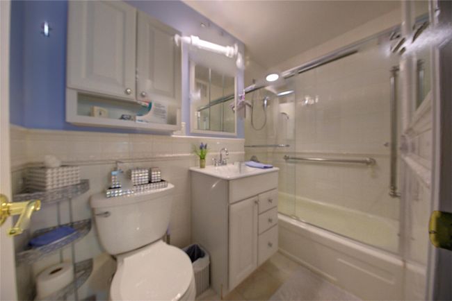 Full bathroom with toilet, shower / bath combination with glass door, and tile walls | Image 16