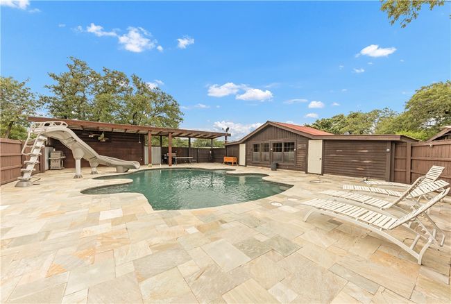 View of pool featuring a water slide, a fenced backyard, a patio area, an outbuilding, and a storage structure | Image 26