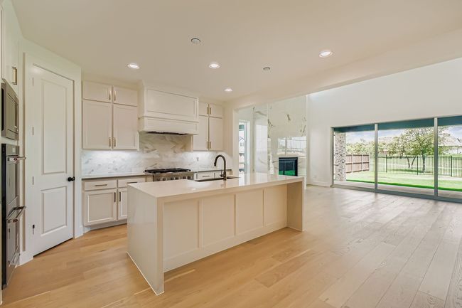 Kitchen with decorative backsplash, a kitchen island with sink, white cabinets, light wood finished floors, and recessed lighting | Image 8