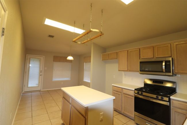 Kitchen with stainless steel appliances, light tile patterned floors, decorative backsplash, a center island, and light countertops | Image 5
