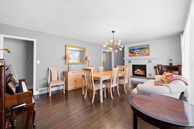 Dining space featuring dark wood-style flooring, visible vents, baseboards, a glass covered fireplace, and an inviting chandelier | Image 6