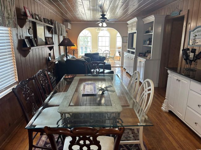 Dining area with a ceiling fan, dark wood-style flooring, wood walls, a wall mounted air conditioner, and wood ceiling | Image 13