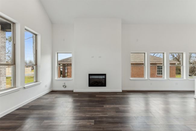 Unfurnished living room with a glass covered fireplace, dark wood-type flooring, and high vaulted ceiling | Image 12