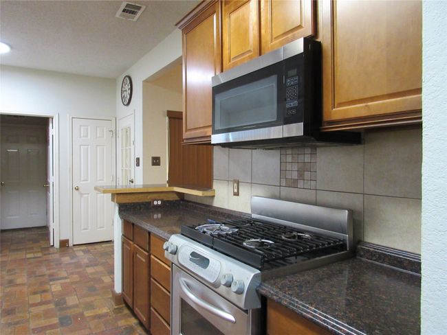 Kitchen featuring brown cabinets, stainless steel appliances, visible vents, brick floor, and decorative backsplash | Image 6