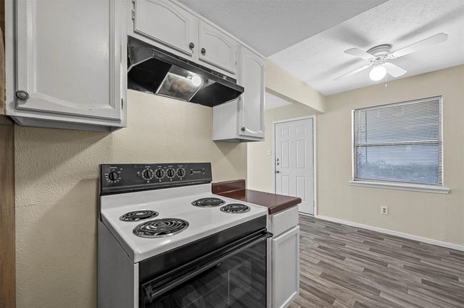 Kitchen with electric range, under cabinet range hood, white cabinets, ceiling fan, and wood finished floors | Image 6