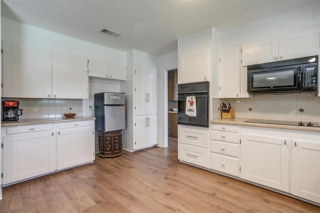 Kitchen with black appliances, backsplash, light wood-type flooring, white cabinetry, and a textured ceiling | Image 19