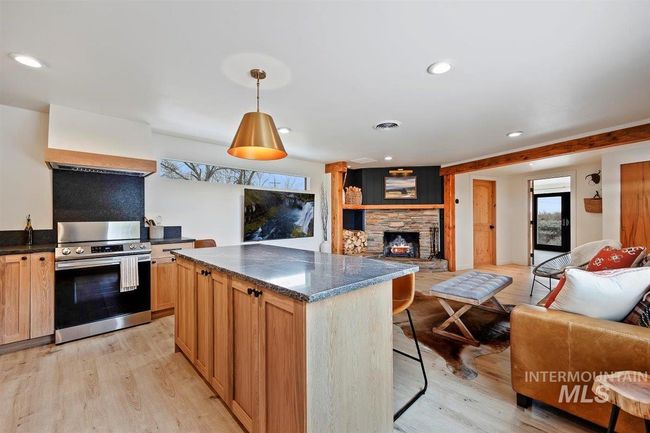 Kitchen with stainless steel range with electric cooktop, open floor plan, light wood-style floors, a stone fireplace, and a kitchen bar | Image 36