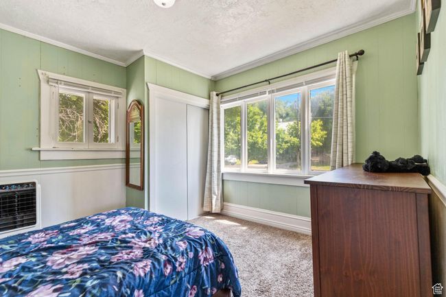 Carpeted bedroom featuring crown molding, multiple windows, a textured ceiling, a closet, and a decorative wall | Image 12