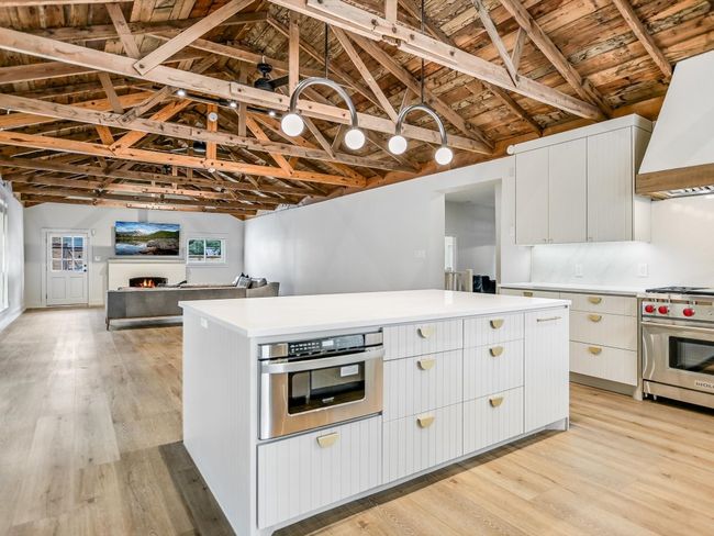 Kitchen with stainless steel appliances, a lit fireplace, light countertops, custom exhaust hood, and light wood finished floors | Image 5
