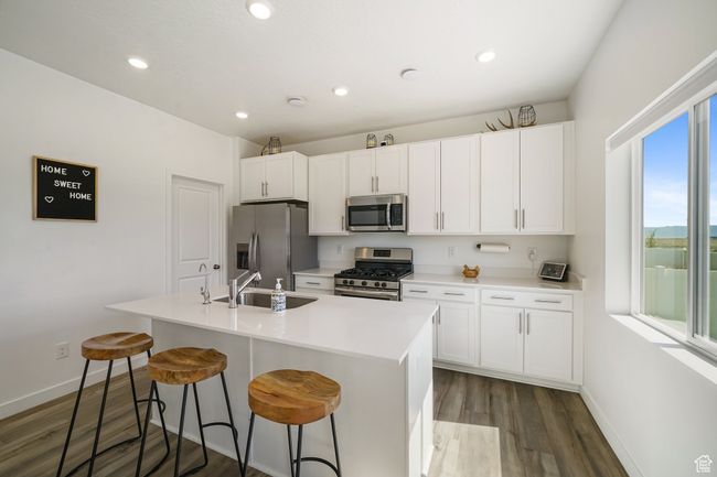 Kitchen with appliances with stainless steel finishes, baseboards, dark wood-style flooring, an island with sink, and a sink | Image 13