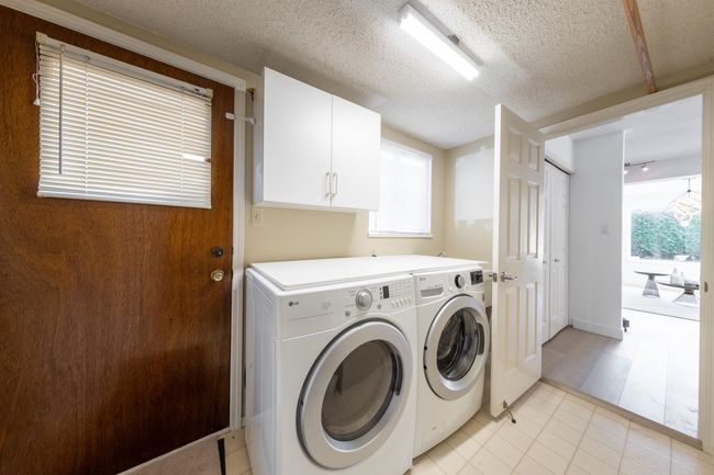 Washroom featuring light tile patterned flooring, washing machine and dryer, a textured ceiling, and cabinet space | Image 33