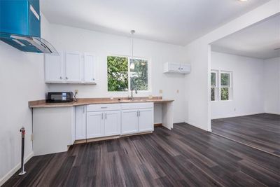 Kitchen featuring island exhaust hood, decorative light fixtures, sink, dark wood-type flooring, and white cabinets | Image 2