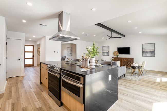 Kitchen with island exhaust hood, stainless steel electric range, light wood-style flooring, visible vents, and vaulted ceiling with beams | Image 5