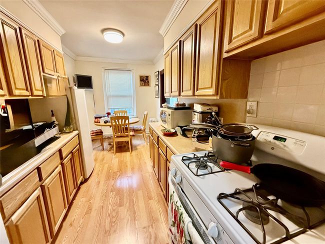 Kitchen featuring white appliances, light countertops, light wood-style floors, ornamental molding, and decorative backsplash | Image 7