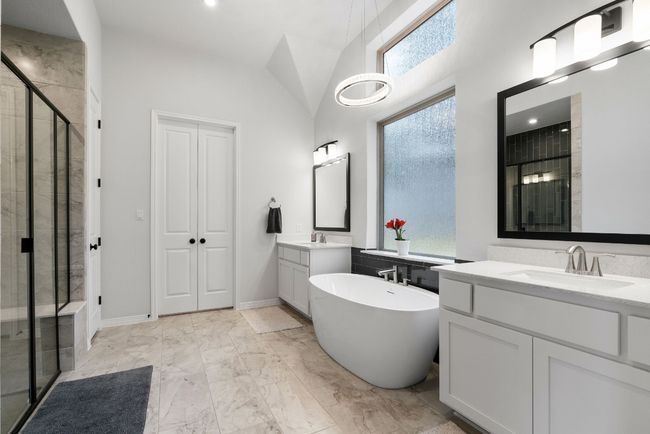 This spa-like primary bathroom contains tile flooring, a deep free-standing garden tub, and separated dual vanities with framed mirrors. | Image 19