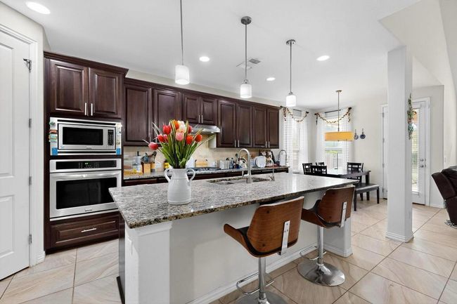 Kitchen featuring a ceiling fan, tasteful backsplash, a tile fireplace, dark brown cabinets, and an island with sink | Image 10