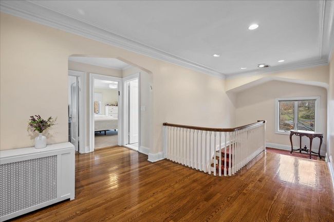 Hall with an upstairs landing, crown molding, baseboards, wood finished floors, and radiator | Image 10