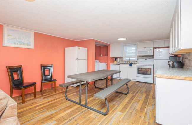 Kitchen with white appliances, washing machine and dryer, light countertops, and white cabinetry | Image 11