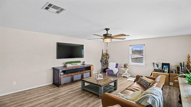 Living area with light wood-type flooring, baseboards, a textured ceiling, visible vents, and ceiling fan | Image 24