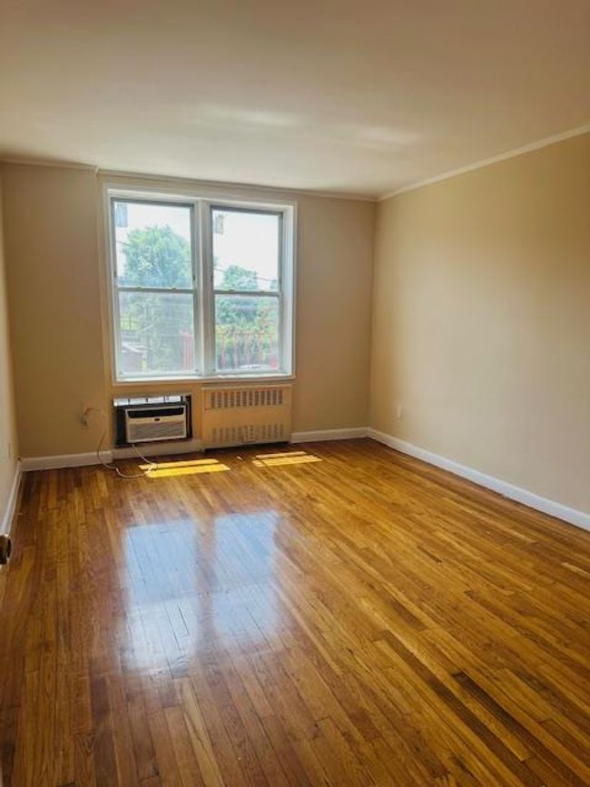Empty room with radiator heating unit, wood-type flooring, crown molding, and a wall mounted AC | Image 6