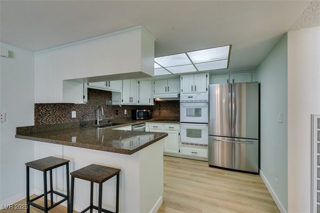 Kitchen with appliances with stainless steel finishes, under cabinet range hood, a peninsula, tasteful backsplash, and light wood-type flooring | Image 24