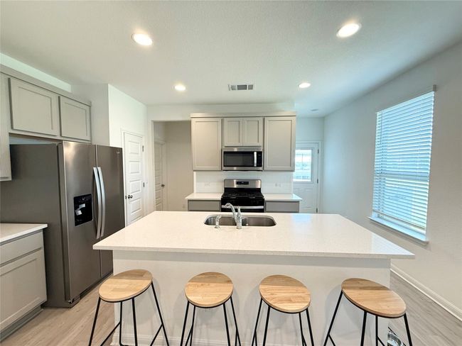 Kitchen with appliances with stainless steel finishes, light wood-style flooring, a sink, a kitchen bar, and an island with sink | Image 12