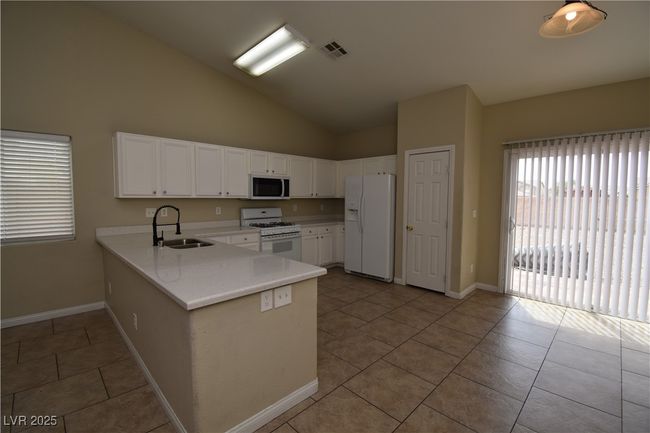 Kitchen with a sink, white appliances, light countertops, a peninsula, and visible vents | Image 7