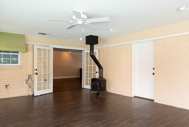 Unfurnished living room with brick wall, a wood stove, wood finished floors, a ceiling fan, and french doors | Image 30
