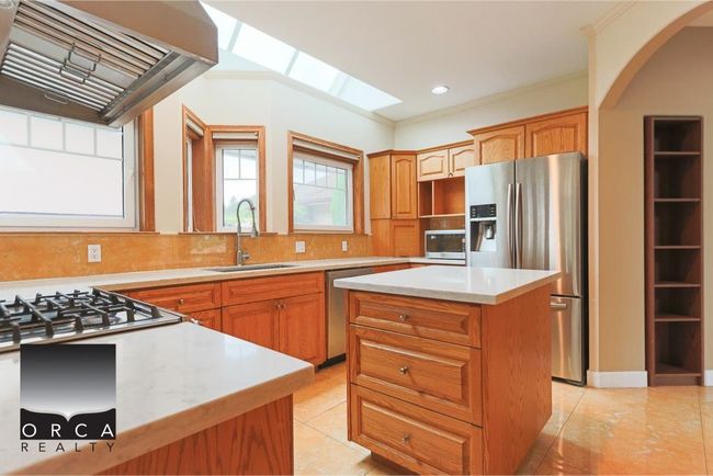 Kitchen with stainless steel appliances, arched walkways, a kitchen island, light countertops, and custom range hood | Image 9