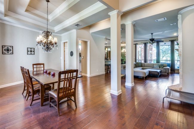 Dining space featuring decorative columns, ornamental molding, a ceiling fan, a tray ceiling, and dark wood-style floors | Image 27
