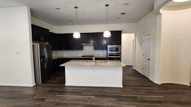 Kitchen with appliances with stainless steel finishes, under cabinet range hood, light stone counters, backsplash, and an island with sink | Image 8
