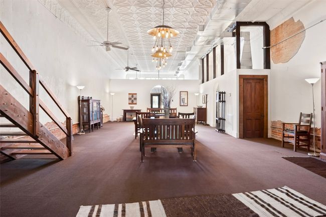 Dining room with ceiling fan with notable chandelier, carpet floors, a high ceiling, and stairway | Image 10