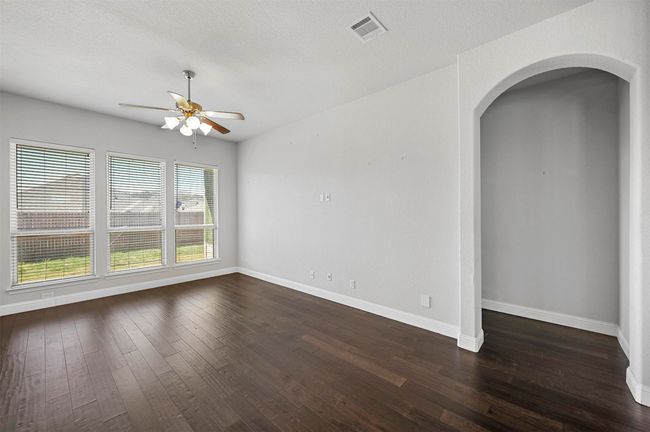 Empty room with visible vents, baseboards, ceiling fan, arched walkways, and dark wood-style flooring | Image 11