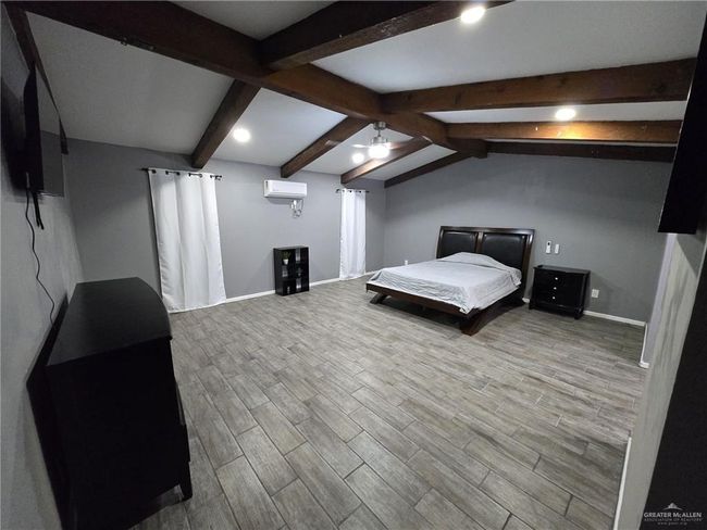 Bedroom featuring an AC wall unit, wood finished floors, and baseboards | Image 5