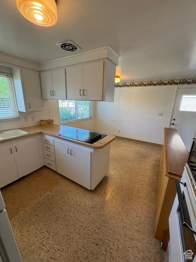 Kitchen with black electric cooktop, white cabinets, range with gas cooktop, light countertops, and a peninsula | Image 5