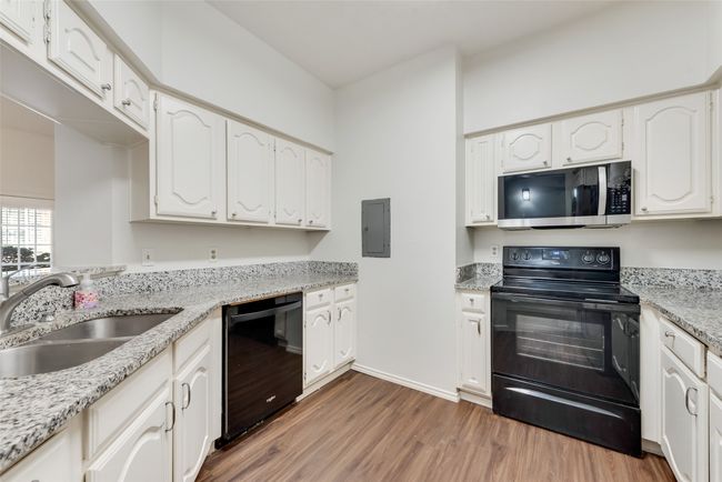 Kitchen with black appliances, light wood finished floors, white cabinetry, light stone counters, and electric panel | Image 9