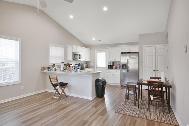Kitchen featuring stainless steel appliances, high vaulted ceiling, a peninsula, white cabinets, and light wood-style flooring | Image 16