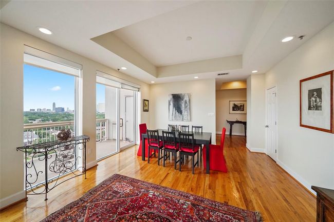 Bright dining area with hardwood floors, modern recessed lighting, and large windows offering city views. Features two glass door leading to a balcony. | Image 10