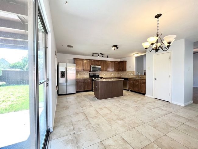 Kitchen with stainless steel appliances, decorative backsplash, a chandelier, a center island, and decorative light fixtures | Image 13