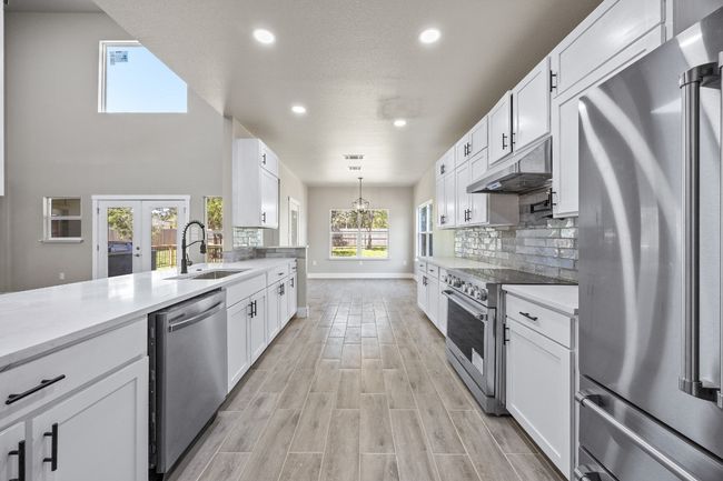 Kitchen featuring backsplash, high end appliances, white cabinets, under cabinet range hood, and a sink | Image 6