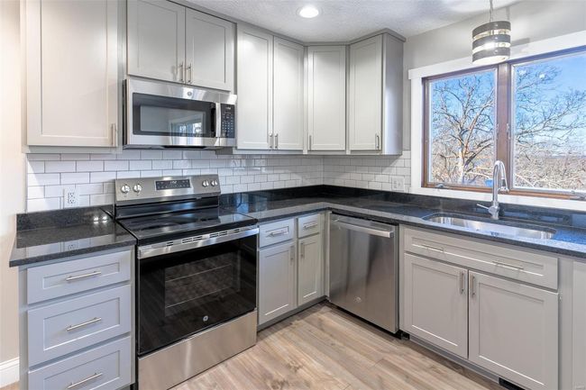 Kitchen with sink, hanging light fixtures, dark stone counters, a textured ceiling, and appliances with stainless steel finishes | Image 43