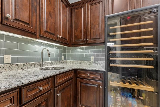 Kitchen featuring backsplash, light stone countertops, a sink, and wine cooler | Image 24