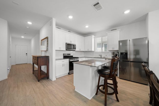 The kitchen features crisp white cabinets with silver hardware, offering a fresh and modern look.An island with a breakfast bar adds extra prep space and casual seating for everyday meals. | Image 9