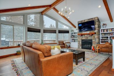 Living room featuring light hardwood flooring, a chandelier, built in features, beamed ceiling, and a stone fireplace | Image 1