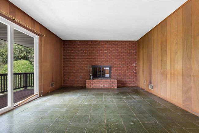 Unfurnished living room with wooden walls, visible vents, and a brick fireplace | Image 16