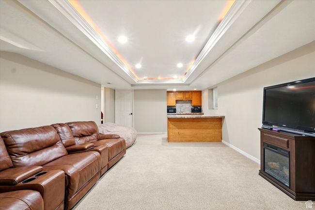 Living area with light colored carpet, a raised ceiling, recessed lighting, a glass covered fireplace, and bar | Image 42